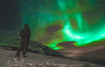 Image of person standing in snow, looking at the Northern Lights in the sky