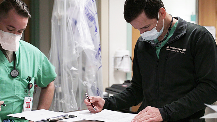 Image of Medical personnel wearing masks, looking at paperwork on desk.
