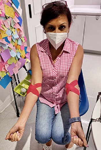 Woman wearing mask, holding out both arms with red tape at elbows