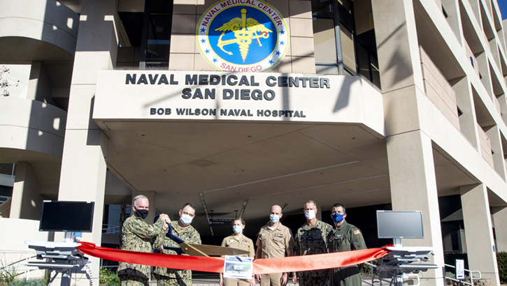 Image of Military personnel wearing face mask standing in front of the Naval Medical Center in San Diego cutting a red ribbon.