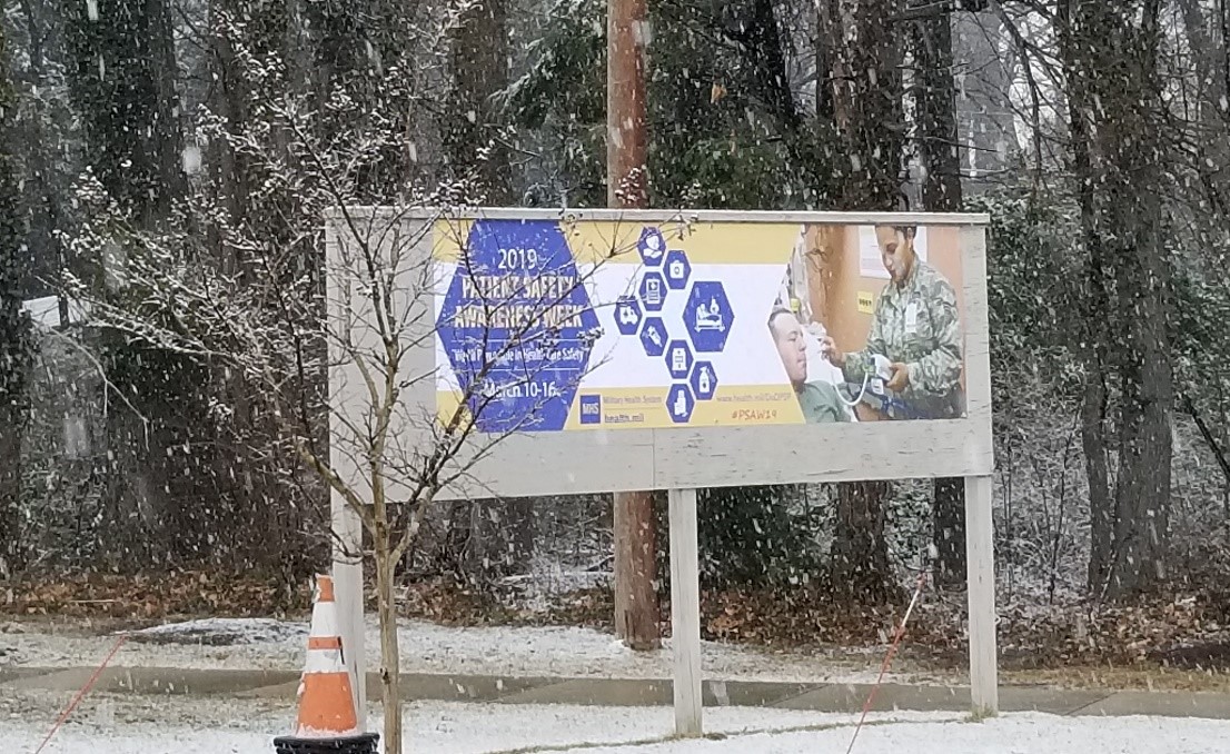 Link to Photo: A Patient Safety Awareness Week parking lot banner hangs at the main entrance of the Defense Health Agency in Falls Church, Virginia during the week of 10-16 March 2019, showing that “We All Play a Role in Healthcare Safety”. 